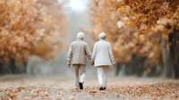 Elderly couple walking together on autumn path with golden fall foliage, holding hands in peaceful park setting for retirement and love concepts.