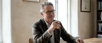Confident mature businessman with glasses sitting at office desk, professional executive in suit planning strategy during corporate meeting or consultation session.