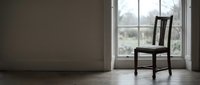Wooden chair positioned by large window in minimalist interior space with neutral walls and natural light, suitable for home decor and design projects.
