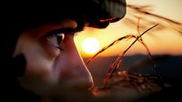 Young woman profile silhouette at golden hour sunset with warm lighting and grass elements creating dreamy atmospheric outdoor portrait scene.