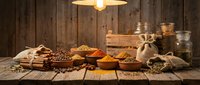 Rustic wooden table displays colorful spices in bowls and burlap sacks with glass jars and warm pendant lighting creating cozy kitchen atmosphere.