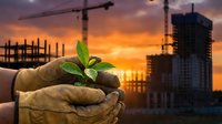 Worker in work gloves holding green seedling sprout at construction site with cranes and building framework at sunset, symbolizing sustainable development and eco-friendly growth.