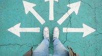 Person in sneakers standing at crossroads with white directional arrows painted on cracked turquoise pavement showing multiple path choices for decision making.