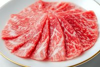 Fresh marbled beef slices arranged in fan pattern on white plate with gold rim, showing premium meat texture and intricate fat marbling pattern.