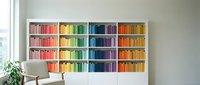Modern home library with colorful books arranged by rainbow spectrum on white built-in shelves creating organized reading space for interior design.