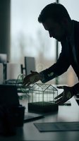 Middle-aged male professional examining miniature greenhouse with glowing leaf icons, symbolizing sustainable business practices and eco-friendly corporate innovation in modern office environment.
