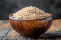 Raw brown sugar crystals in wooden bowl on rustic table against dark background, macro food photography for cooking and healthy lifestyle concepts.