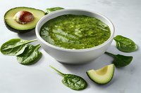 Fresh green smoothie bowl with spinach leaves and sliced avocado on light background, healthy breakfast or detox drink preparation.