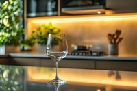 Empty wine glass on modern kitchen counter with warm ambient lighting and blurred background showing contemporary home interior design elements.