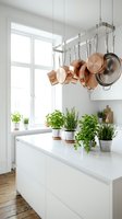 Modern white kitchen interior with hanging copper pots and fresh herb plants on marble countertop, bright Scandinavian style home decor.