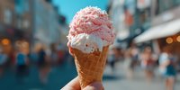 Pink strawberry ice cream cone with sprinkles held against blurred city street background. Summer dessert treat for cafes and food marketing campaigns.