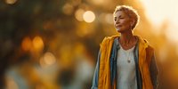 Senior woman with short gray hair in yellow jacket enjoying golden hour sunset light, contemplative expression perfect for wellness and aging concepts.