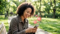 Happy young African American woman with curly hair using smartphone in park, receiving social media likes and notifications outdoors.