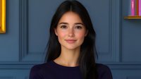 Young Asian woman with long dark hair and natural makeup wearing navy blue sweater smiling warmly against blue wall background, professional headshot style portrait.