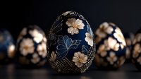 Decorative Easter egg with delicate floral pattern in gold and blue on dark background, traditional folk art design with blurred similar eggs behind.