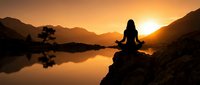 Woman in lotus position meditating on rock by calm lake at golden sunrise, surrounded by mountains. Silhouette yoga practice for wellness, mindfulness and spiritual growth.