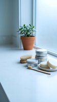 Eco-friendly bathroom essentials with natural soap, wooden brushes and metal containers on white windowsill with green plant for sustainable living.