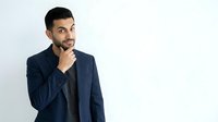 Young Middle Eastern man in navy blazer and dark shirt, hand to chin in thoughtful pose, isolated on white background for business and corporate design use.