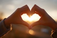 Hands forming heart shape silhouette against golden sunset sky creating romantic love symbol with warm sunlight glowing through fingers for Valentine's Day.