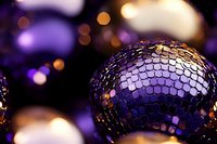 Shimmering disco ball with purple and gold reflections creates magical party atmosphere against dark background with festive bokeh lights.
