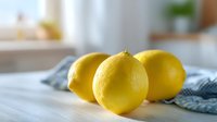 Fresh yellow lemons on kitchen table with blue checkered napkin, bright natural lighting creates vibrant citrus scene for cooking or healthy recipes.