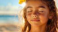 Young mixed race girl with closed eyes and gentle smile enjoying warm sunlight at beach, backlit portrait with golden hour glow and peaceful expression.