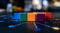 Colorful wooden blocks arranged in row on dark surface with dotted pattern, showing vibrant blue, green, orange, purple and red cubes in selective focus.