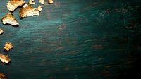 Gold leaf fragments scattered on dark emerald green wooden background with rich texture and dramatic lighting, creating luxurious artistic composition.