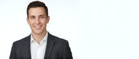 Young professional businessman in dark suit smiling confidently on white background, corporate headshot for business presentations and marketing materials.