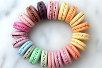 Colorful French macarons arranged in rainbow circle pattern on marble background, featuring pastel pink, purple, yellow, green, and blue varieties with delicate filling.