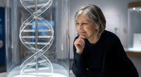 Senior Caucasian female scientist examining DNA double helix model in modern laboratory, genetic research and biotechnology study for medical advancement.