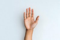 Raised open palm of young Asian woman showing stop gesture against light gray background, minimal composition for social concepts and communication.