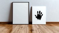 Black handprint on white canvas next to empty frame on wooden floor against white wall, minimalist art composition for modern interior design and gallery display.