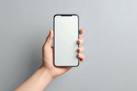 Female hand holding modern smartphone with blank white screen against gray background, perfect for app or website mockup presentation.