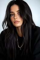 Young Hispanic woman with long dark hair wearing black hoodie and necklace against light background, natural makeup look and soft lighting creating moody portrait.