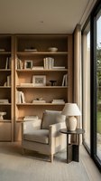 Modern reading nook with wooden built-in shelving, cream upholstered armchair, ceramic table lamp, and natural light from large windows. Interior design for home decor and lifestyle publications.