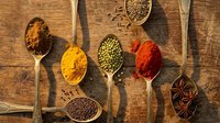Colorful spices and herbs in wooden spoons on rustic wood background. Cooking ingredients including turmeric, paprika, cumin, and star anise for culinary recipes.