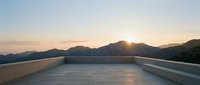 Sunrise over mountain landscape viewed from modern concrete rooftop terrace with minimalist railing, ideal for architecture and travel design projects.