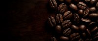 Roasted coffee beans scattered on dark wooden surface with copy space for café, beverage, and food industry designs.