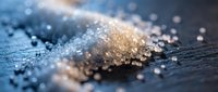 Close-up of sparkling salt crystals scattered on dark wooden surface with warm and cool lighting creating bokeh effect.