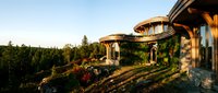 Futuristic eco-friendly residential architecture with curved organic design nestled in forested landscape during golden hour, sustainable living concept for environmental design projects.