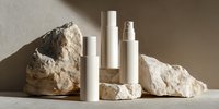 White cosmetic bottles on natural stone podiums against neutral background, minimalist beauty product presentation for skincare and wellness branding.
