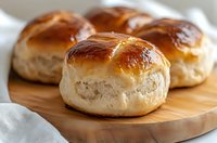 Fresh homemade dinner rolls with golden brown tops and soft texture served on wooden cutting board, close up view of traditional bread baking.