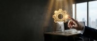 Businessman touching glowing gear icon in modern office workspace, representing innovation, technology integration, and digital transformation strategy for corporate solutions.