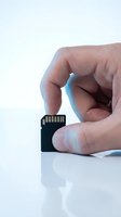 Close-up of male hand holding small black memory card with gold contacts against white background. Storage device for photography and digital data.