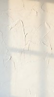 Cracked white paint peeling off wall surface showing weathered aged texture with natural wear patterns for vintage interior design backgrounds.