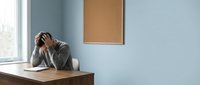 Stressed businessman holding head in hands at office desk showing workplace burnout and mental health challenges in modern corporate environment.