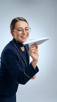 Young professional woman with fair complexion, dark hair, and glasses wearing navy blazer holding paper airplane, smiling against white background for business and startup concepts.