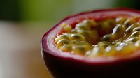 Fresh passion fruit cut in half showing juicy pulp and seeds with vibrant purple skin, extreme close up macro photography on blurred background.