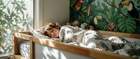 Young woman with brown hair sleeping peacefully in wooden bed with tropical jungle wallpaper featuring colorful parrots and lush green foliage in sunlit bedroom.